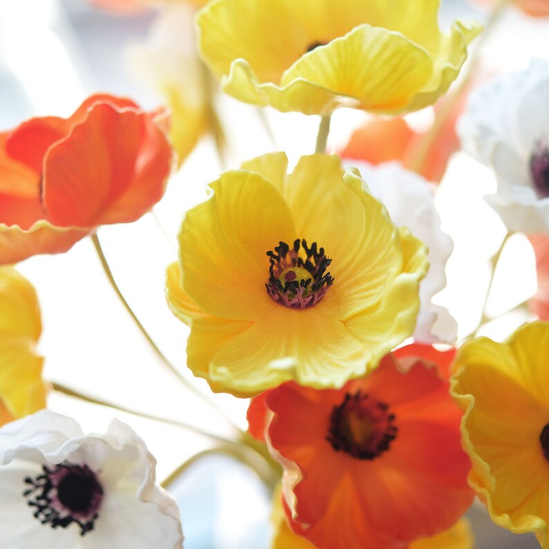 Puede incluir: Un ramo de flores de seda con p&eacute;talos de color naranja, amarillo y blanco. Las flores est&aacute;n dispuestas en un jarr&oacute;n y tienen un aspecto realista.