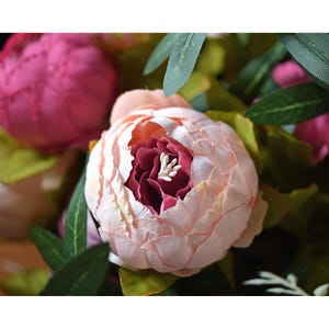 Puede incluir: Un ramo de peon&iacute;as artificiales de color rosa y blanco con hojas verdes. Las peon&iacute;as tienen un aspecto en capas y con volantes.