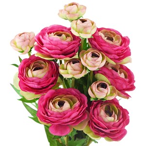 May include: A bouquet of artificial ranunculus flowers in shades of pink and cream. The flowers have multiple layers of petals, with some blooms fully open and others in bud form. Green leaves provide contrast against the white background.
