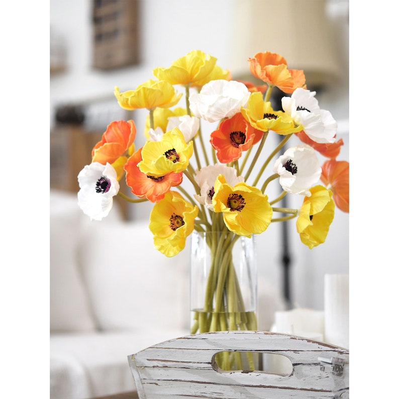 Puede incluir: Un ramo de amapolas artificiales en un jarr&oacute;n de vidrio transparente. Las flores son una mezcla de blanco, amarillo y naranja.
