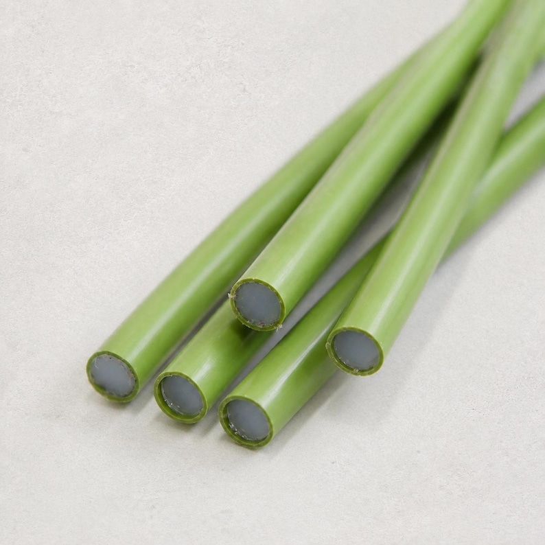 May include: A collection of four cylindrical rods featuring a smooth, matte olive green exterior coating and a light gray, circular core visible at the ends. The rods are arranged in a parallel, slightly overlapping cluster, showcasing their uniform shape.