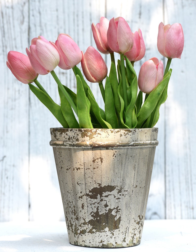 K&ouml;nnte beinhalten: Ein Strau&szlig; rosa Tulpen in einem wei&szlig;en, abgenutzten Topf. Der Topf hat ein rustikales, gealtertes Aussehen mit brauner und wei&szlig;er Farbe.