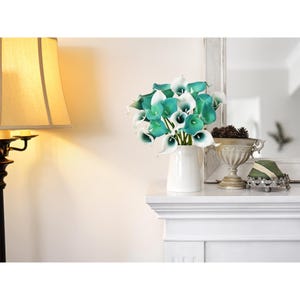 Peut inclure: Un bouquet de callas artificiels pr&eacute;sentant un d&eacute;grad&eacute; de couleurs blanc et sarcelle, dispos&eacute; dans un pichet en c&eacute;ramique blanche. Les fleurs ont des p&eacute;tales lisses et incurv&eacute;s ainsi que des spadices centraux bien visibles.