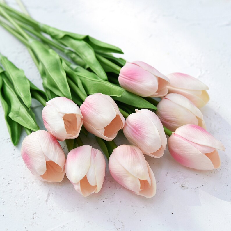 May include: A bouquet of pink artificial tulips with green stems. The tulips are arranged in a cluster, with the stems extending out from the center.
