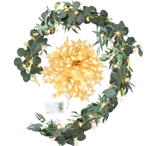 May include: A decorative garland with green eucalyptus leaves and small star-shaped lights. A cluster of star-shaped lights is in the center. A battery pack is visible, suggesting the lights are battery-operated.