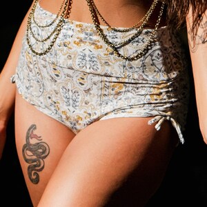 Puede incluir: Un bikini de color blanco y dorado con un tatuaje de serpiente en el muslo.