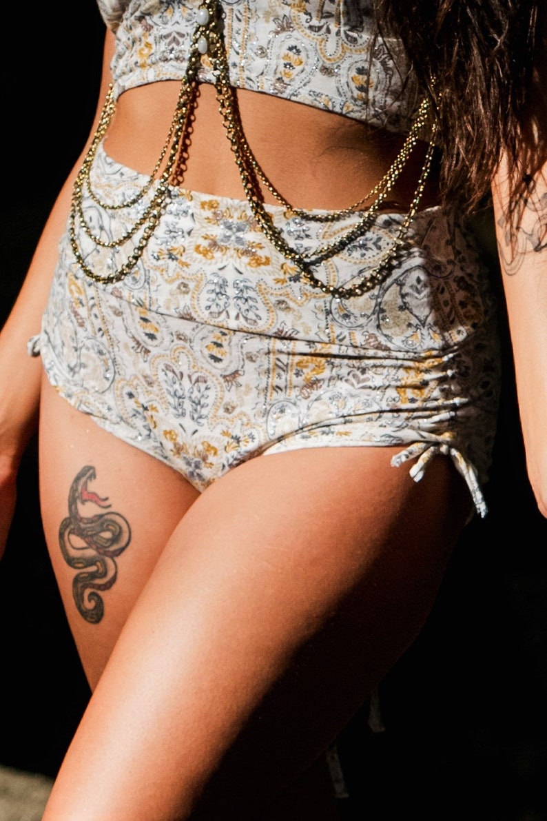 Puede incluir: Un bikini de color blanco y dorado con un tatuaje de serpiente en el muslo.