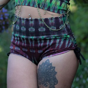 Puede incluir: Pantalones cortos de color negro y verde con estampado, con un tatuaje de mandala en blanco y negro en la pierna. Los pantalones cortos tienen un cord&oacute;n en el lateral y un cintur&oacute;n de cadena dorada.