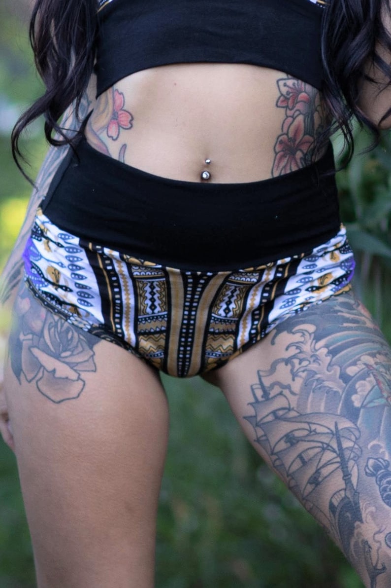 Puede incluir: Pantalones cortos de cintura alta con estampado blanco y negro y cintura negra. Los pantalones cortos tienen un dise&ntilde;o geom&eacute;trico con detalles dorados. La modelo lleva los pantalones cortos con un top corto negro.
