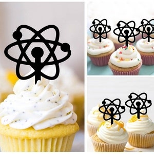 以下が含まれることがあります： 黒い原子のカップケーキトッパー。トッパーは黒いアクリル製で、スタイリッシュな原子のデザインが施されています。トッパーは、白いフロスティングをかけたカップケーキの上に載せられています。