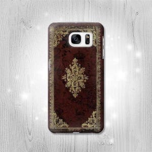 Può includere: Una custodia per telefono marrone con un design dorato ornato. La custodia ha un ritaglio per l'obiettivo della fotocamera.