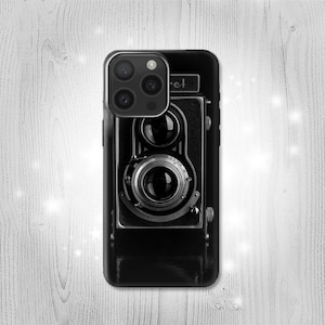 Puede incluir: Carcasa de teléfono en blanco y negro con un diseño de cámara vintage. La cámara tiene una lente y dos visores.