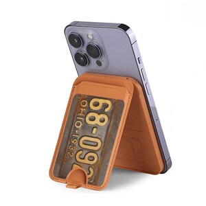 May include: A brown leather phone case with a built-in card holder. The card holder features a vintage-style license plate with the text "68-06" and "OHIO 1932".