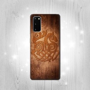 Può includere: Una custodia per telefono in legno marrone con un design intagliato di un nodo celtico. La custodia ha un ritaglio per la fotocamera nero.