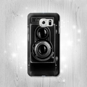 Puede incluir: Carcasa de teléfono en blanco y negro con una cámara vintage con una lente y dos visores. La carcasa tiene un diseño elegante y moderno.