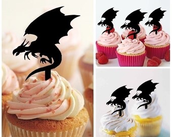May include: Black silhouette dragon cupcake toppers. The toppers are on top of cupcakes with pink frosting and sprinkles. The cupcakes are on a white surface.