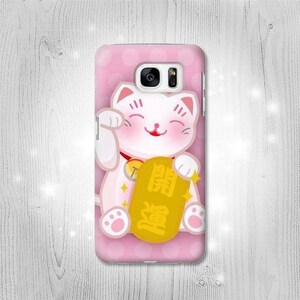 May include: A pink phone case with a white cartoon cat holding a gold coin with Chinese characters. The cat is smiling and has its paw raised in a gesture of good luck.