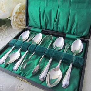 May include: A set of six silver teaspoons and a pair of sugar tongs in a green velvet-lined box.