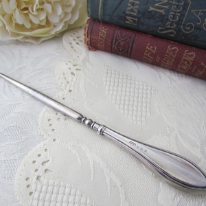 May include: A silver shoe horn with a hook at one end and a rounded, pointed end. The shoe horn has a decorative design and the inscription "925" on the handle.