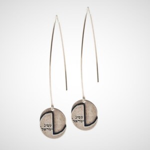 May include: A pair of silver dangle earrings with a round disc charm featuring Hebrew text. The earrings have long, thin wires.