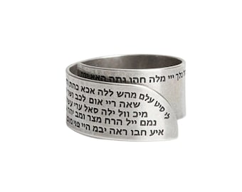 Op de afbeelding: Een zilveren ring met Hebreeuwse tekst gegraveerd op de band. De tekst is in een traditioneel Hebreeuws lettertype en is om de ring gewikkeld.