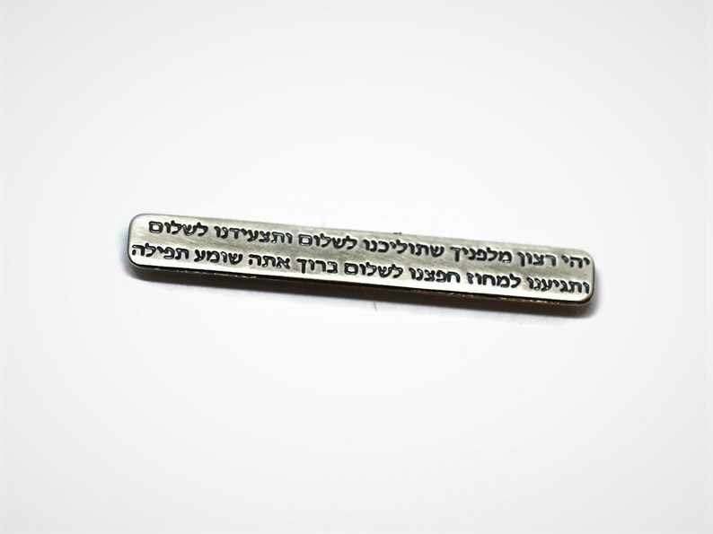 May include: A silver metal bar with Hebrew text engraved on it. The text reads: "יהי רצון מלפניך שתוליכנו לשלום ותצעידנו לשלום ותגיענו למחוז חפצנו לשלום ברוך אתה שומע תפילה"