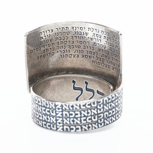 Puede incluir: Un anillo de plata con texto hebreo grabado en la banda y en el interior del anillo. El texto en el interior del anillo dice "אנא בכח גדלת ימינך תתיר צרורה נא גבור, דורשי יחודך כבבת שמרם קבל רנת עמך, שגבנו, טהרנו, נורא חסין קדוש, ברוב טובך נהל עדתך ברכם, טהרם, רחמי צדקתך תמיד נמלם יחיד גאה, לעמך פנה, זוכרי קדושתך שועתנו קבל וּשׁמַע צַעֲקָתֵנוּ, יודע תעלומות:"