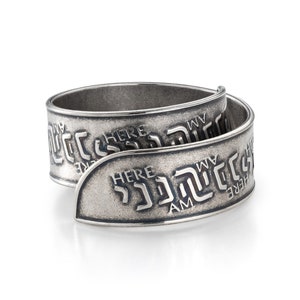 May include: A silver ring with the words "Here I Am" engraved on it in both English and Hebrew.