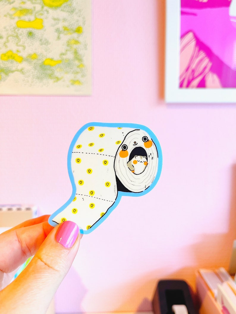 May include: A blue and white sticker of a cartoon animal peeking out of a roll of toilet paper. The animal has a white body, black eyes, and orange cheeks. The toilet paper is white with yellow dots.