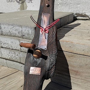 Puede incluir: Un reloj de madera rústico con una esfera de cobre y agujas rojas. El reloj está montado en un trozo de madera a la deriva con una placa de cobre que dice "Lucky Time".