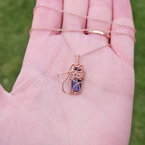 May include: A rose gold necklace with a wire-wrapped pendant featuring a blue gemstone and a heart charm.