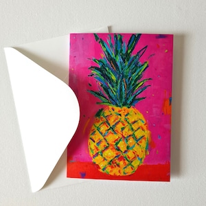 Könnte beinhalten: Eine Grußkarte mit einem impressionistischen Gemälde einer Ananas. Die Ananas ist gelb mit grünen und blauen Akzenten, vor einem leuchtend rosa Hintergrund. Ein weißer Umschlag ist teilweise sichtbar.