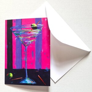 May include: Greeting card with a colourful painting of a martini cocktail, complete with an olive and a red swizzle stick. The background features vertical stripes of pink, purple, and black. A white envelope is included.
