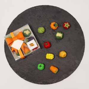 May include: A clear square box containing assorted fruit and vegetable shaped marzipan sweets, tied with a bright orange ribbon and a white tag. Several loose marzipan pieces shaped like pumpkins, corn, and peppers are scattered on a dark slate.