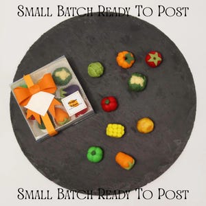 Può includere: Una scatola quadrata trasparente contenente dolcetti di marzapane a forma di verdura, legata con un nastro arancione e un'etichetta con la scritta "Small Batch Ready To Post". Diverse verdure di marzapane sfuse sono disposte accanto alla scatola.
