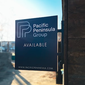 Pode incluir: Uma placa retangular azul escura com o texto "Pacific Peninsula Group" e "AVAILABLE" em letras brancas. A placa está fixada a uma estrutura de madeira. O endereço do site www.pacificpenineula.com é visível na parte inferior.