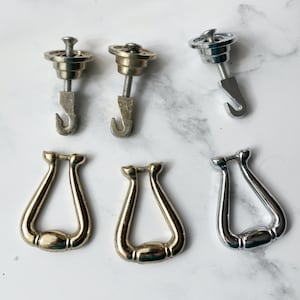 May include: A set of six decorative door hardware pieces. Two are silver hooks with a round base and two are gold hooks with a round base. Two are gold and silver U-shaped door pulls.