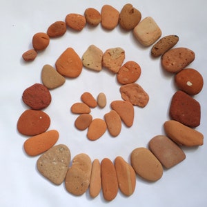 May include: A spiral arrangement of small, smooth, reddish-brown stones on a white background.