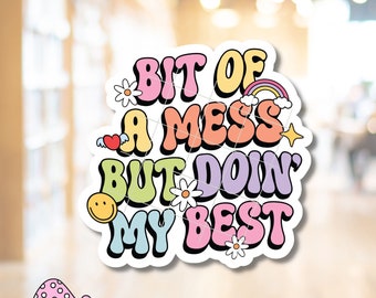 May include: A colorful sticker with the text "Bit of a mess but doin' my best" in a retro font. The sticker features a rainbow, a flower, a heart, a star, and a smiley face.