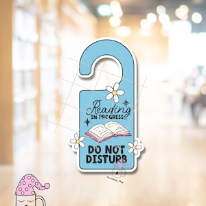May include: A blue door hanger with a white daisy and the text "Reading in Progress... Do Not Disturb". The hanger features a cartoon mug with a pink and white sleep cap.