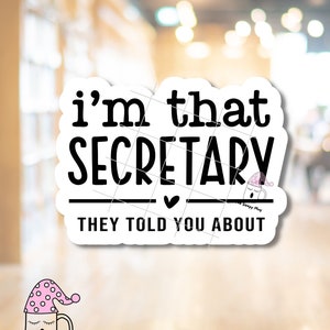 May include: White sticker with black text that reads "i'm that SECRETARY they told you about". A small cartoon mug with a pink and white sleep cap is in the bottom right corner of the sticker. The text "The Sleepy Mug" is below the mug.
