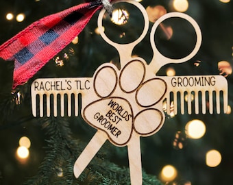 Könnte beinhalten: Weihnachtsbaumschmuck aus Holz in Form eines Hundepfotes mit einer Schere und einem Kamm. Der Anhänger trägt die Aufschrift "World's Best Groomer" und "Rachel's TLC" und "Grooming".