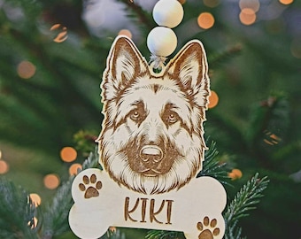 Può includere: Un ornamento natalizio in legno a forma di osso con la testa di un pastore tedesco al centro. La testa del cane è marrone e nera e l'osso è bianco. L'osso ha il nome "KIKI" inciso su di esso e impronte di zampe su entrambi i lati.