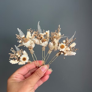 May include: Set of five gold hair pins decorated with dried flowers. The flowers are white and brown and include small daisies and dried grasses.