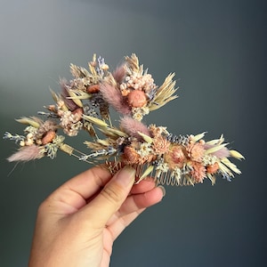 May include: A gold hair comb adorned with dried flowers in shades of pink, beige, and lavender. The comb features a variety of dried flowers, including small pink roses, fluffy white flowers, and dried grasses.