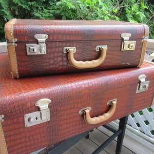 Peut inclure: Deux valises marron vintage empilées. Elles présentent un motif imitation crocodile et des bordures beiges. Chacune a une poignée beige et des fermoirs métalliques. Ces valises, probablement du milieu du XXe siècle, sont un accessoire de voyage classique.