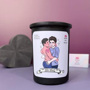 May include: Black candle with a label featuring an illustration of two embracing figures. The label includes the text "SCENT OF A KILLER" and "You better hold on tight, spider monkey."