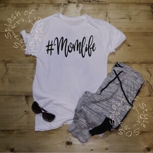 May include: White t-shirt with black text that says "#Momlife". The shirt is paired with gray sweatpants.