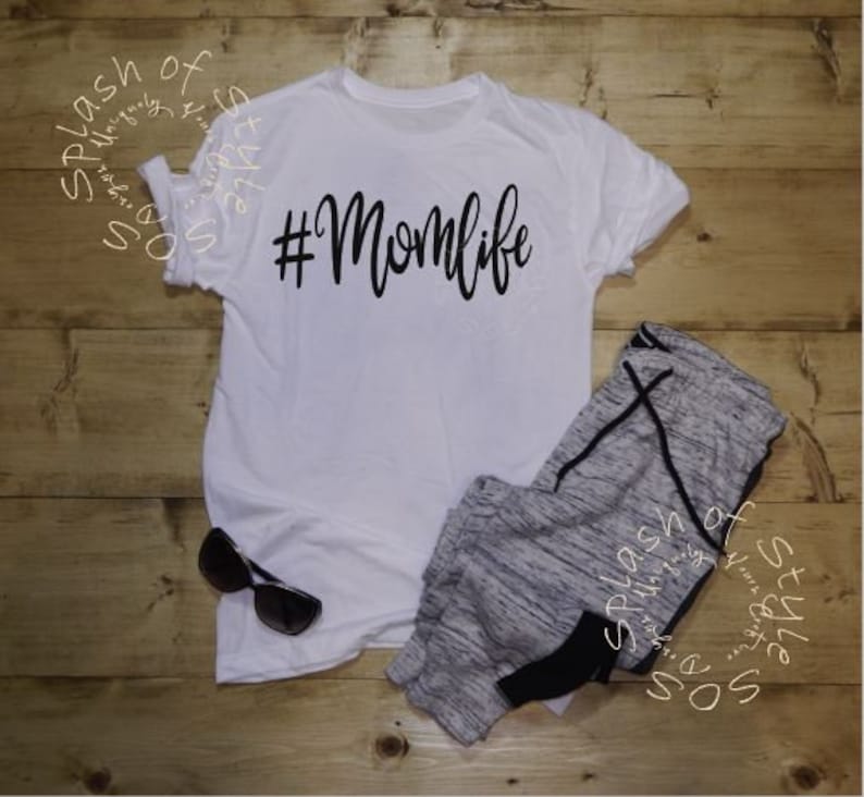 May include: White t-shirt with black text that says "#Momlife". The shirt is paired with gray sweatpants.