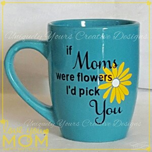 May include: A turquoise ceramic mug with a black and yellow design. The mug has a handle and says "If Moms were flowers I'd pick you".